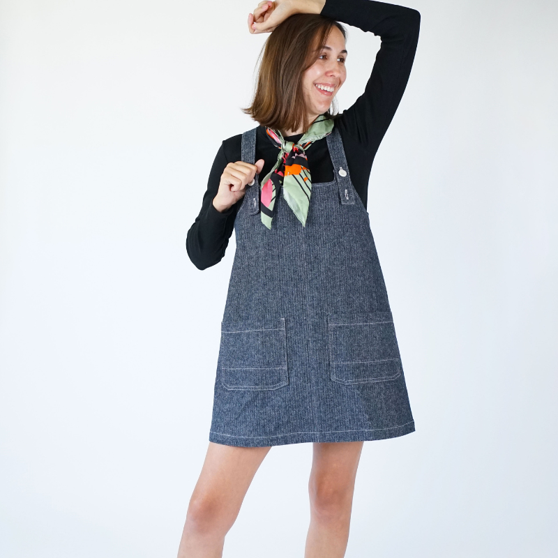 Woman wearing a denim pinafore dress with a plain background