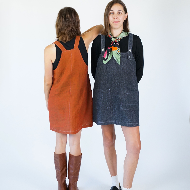 Two women wearing denim pinafore dresses on a white background