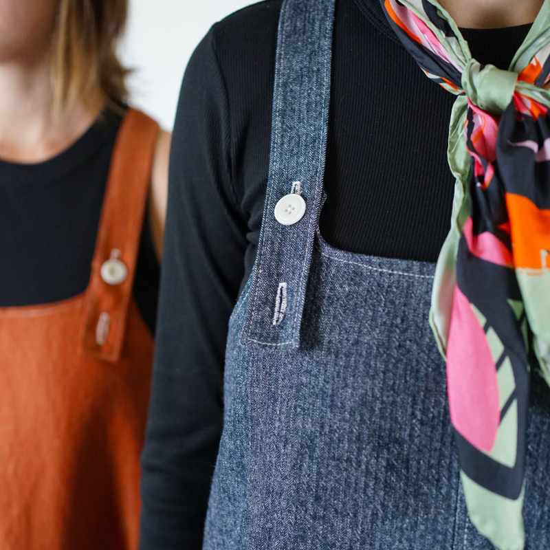 Person wearing a denim apron over a black shirt with a colorful scarf.