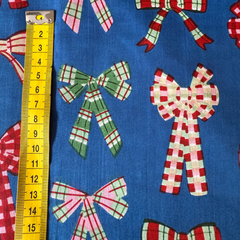 Fabric with checkered bows on a blue background, measured by a yellow ruler.