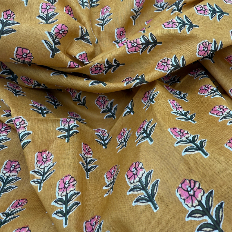 Floral patterned fabric with pink flowers and green leaves on a mustard yellow background