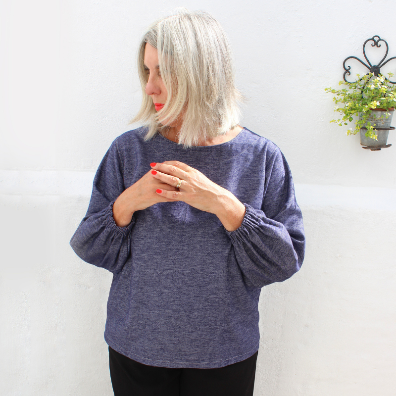 Woman wearing a blue sweater against a white wall with a plant in the background