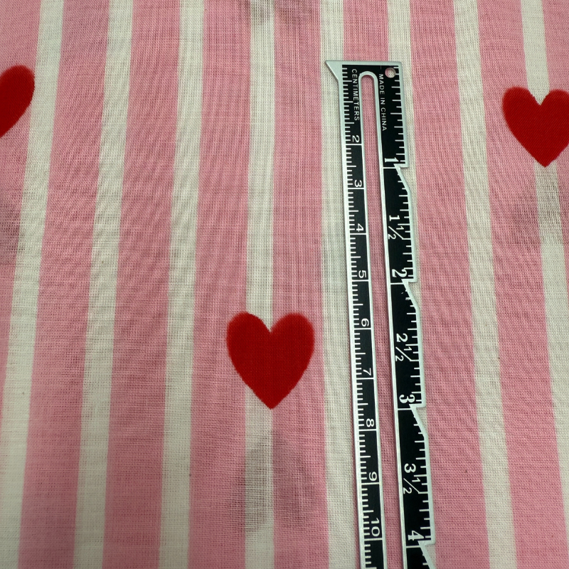 Ruler on a fabric with red heart shapes and pink and white stripes