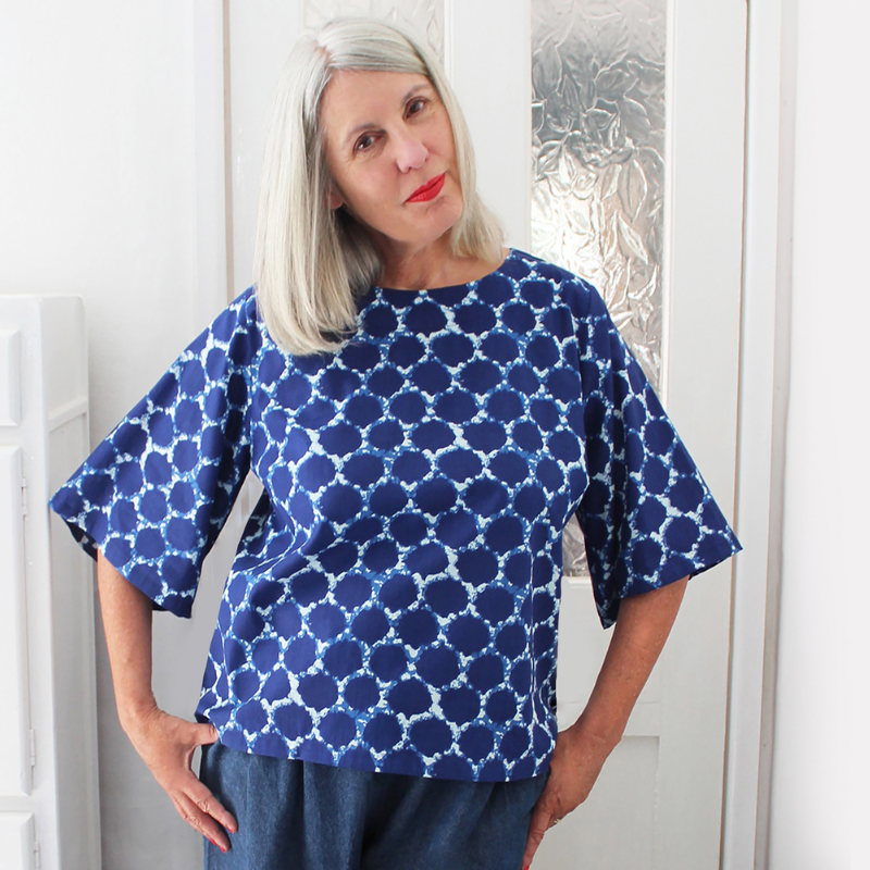Woman wearing a blue patterned top against a white wall