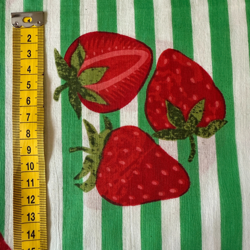 red strawberries with green leaves on a green and white striped fabric background, with a yellow ruler for scale.