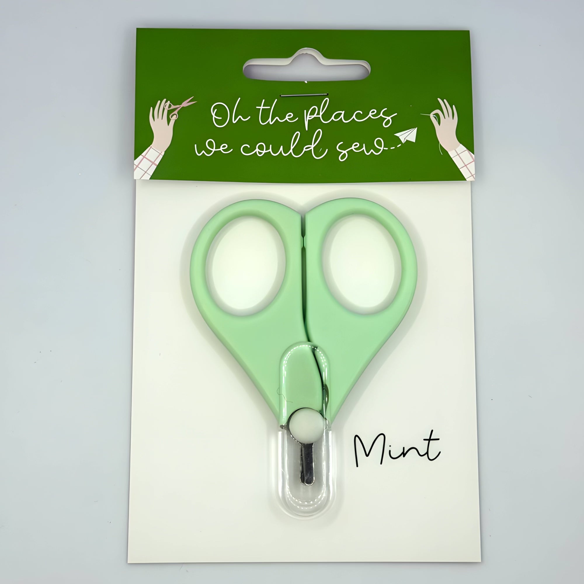 Green scissors in packaging with 'Oh the places we could sew' text on a light gray background