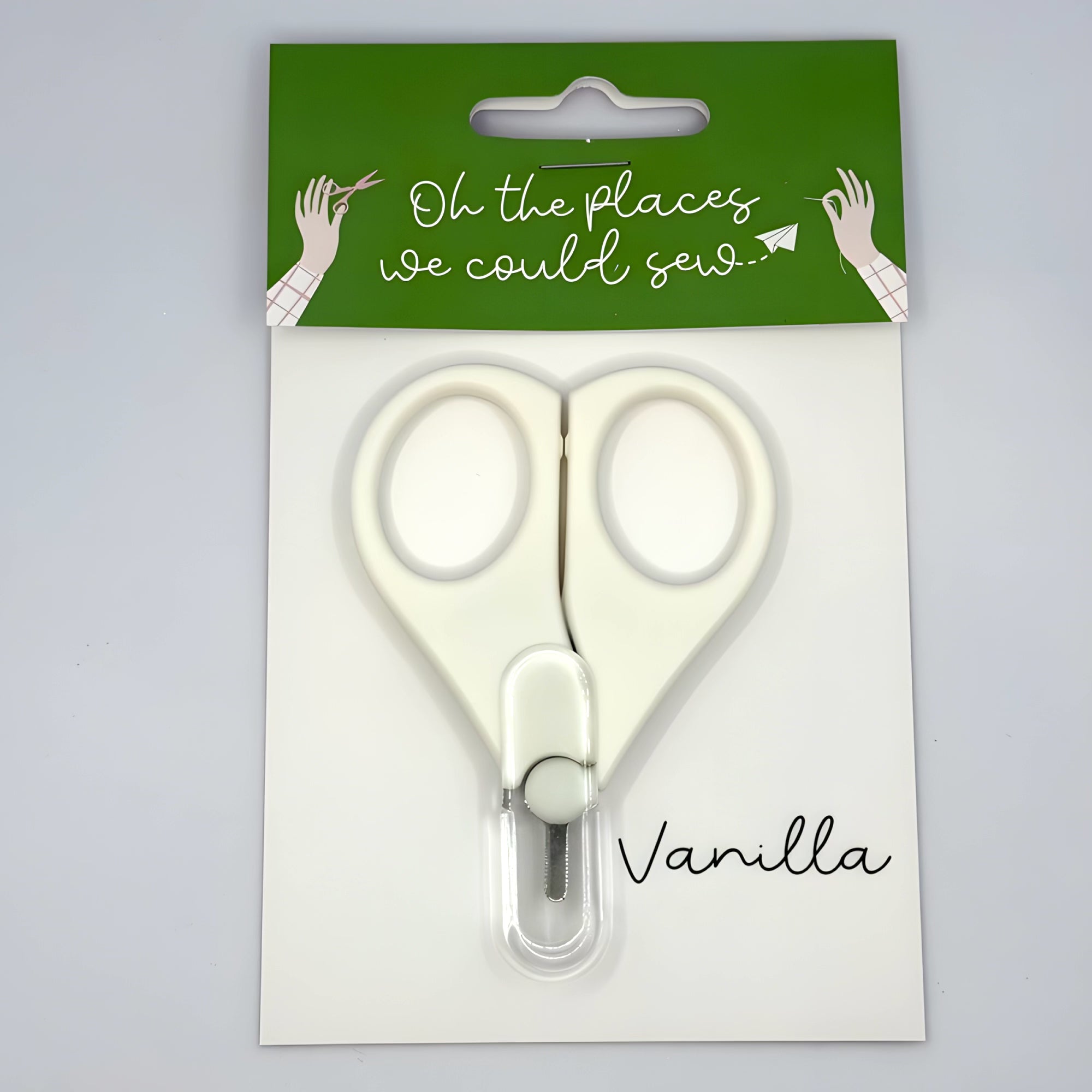 White scissors in packaging with green and white label on gray background