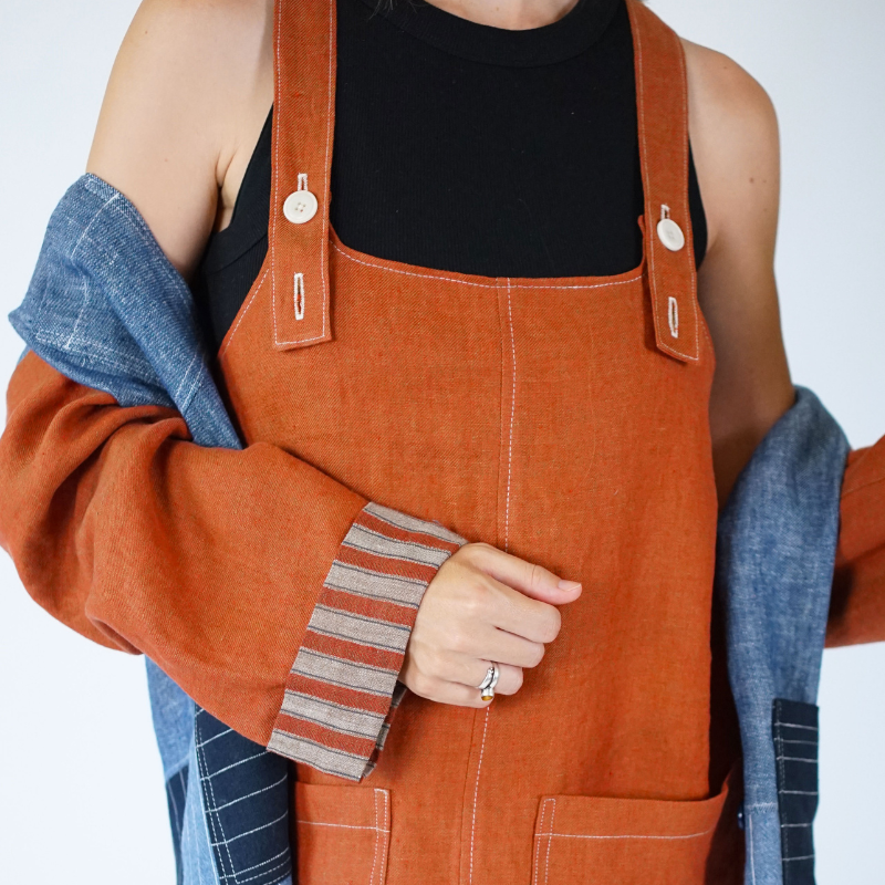 Person wearing an orange denim apron over a black shirt with a white background