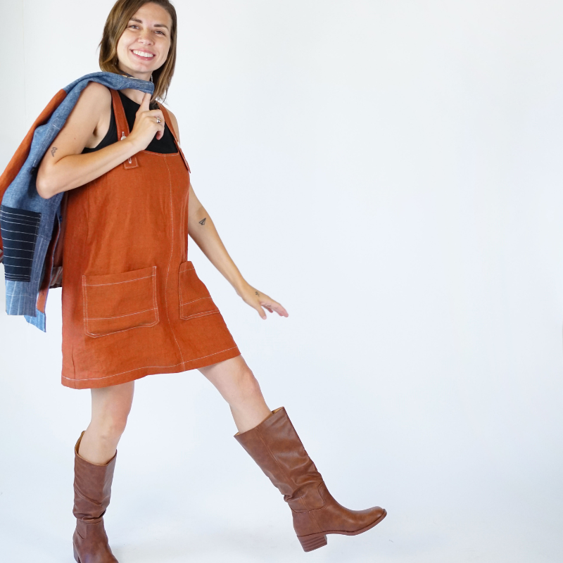Woman wearing a brown pinafore dress and brown boots on a white background