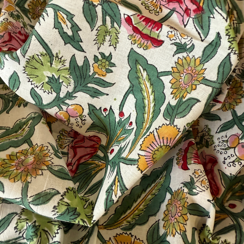 Close-up of floral fabric with green, yellow, and red patterns on a beige background.