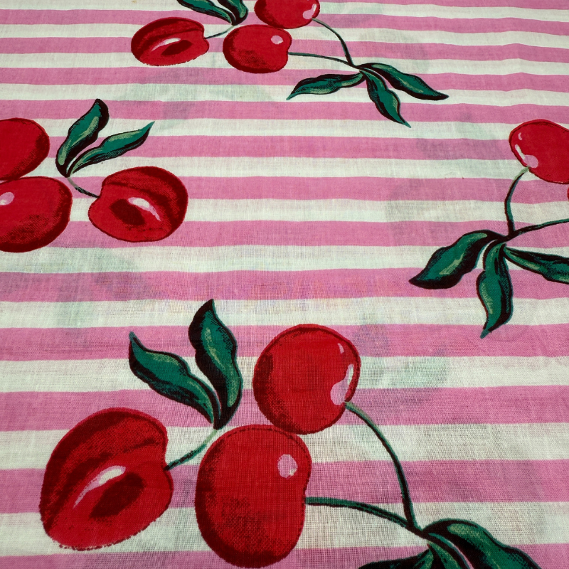 Fabric with red cherries and green leaves on a pink and white striped background