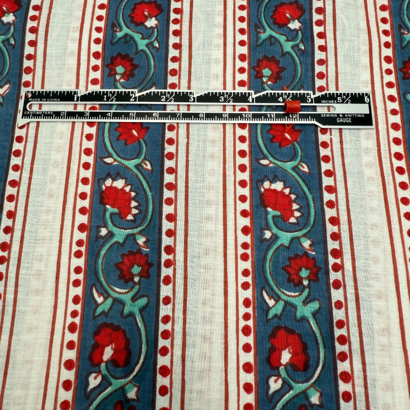 Fabric with red floral patterns on a blue and white striped background, measured by a ruler.