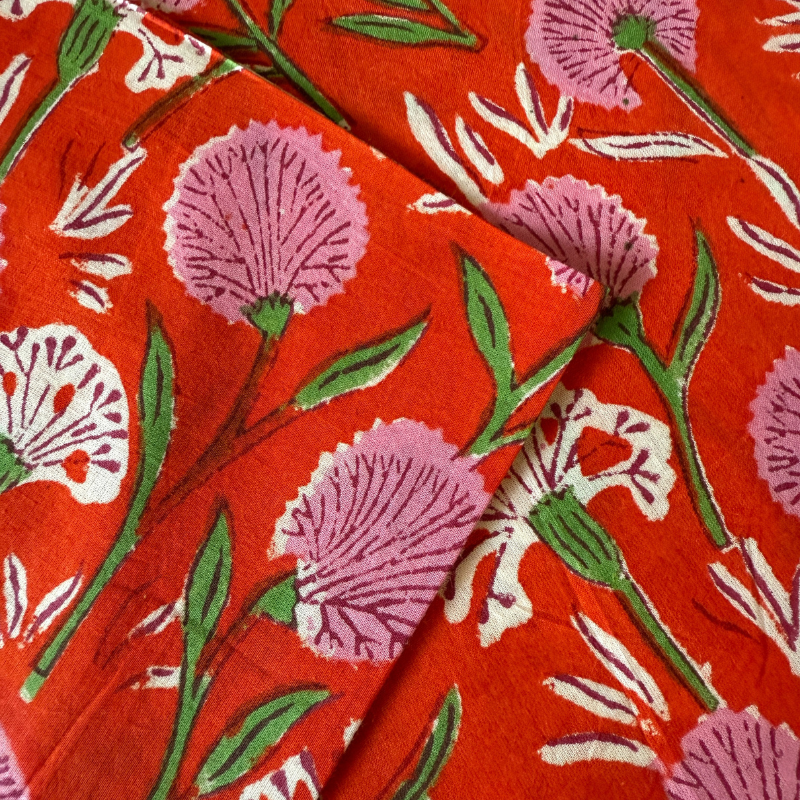 Floral pattern on red fabric with pink flowers, green leaves, and white accents.