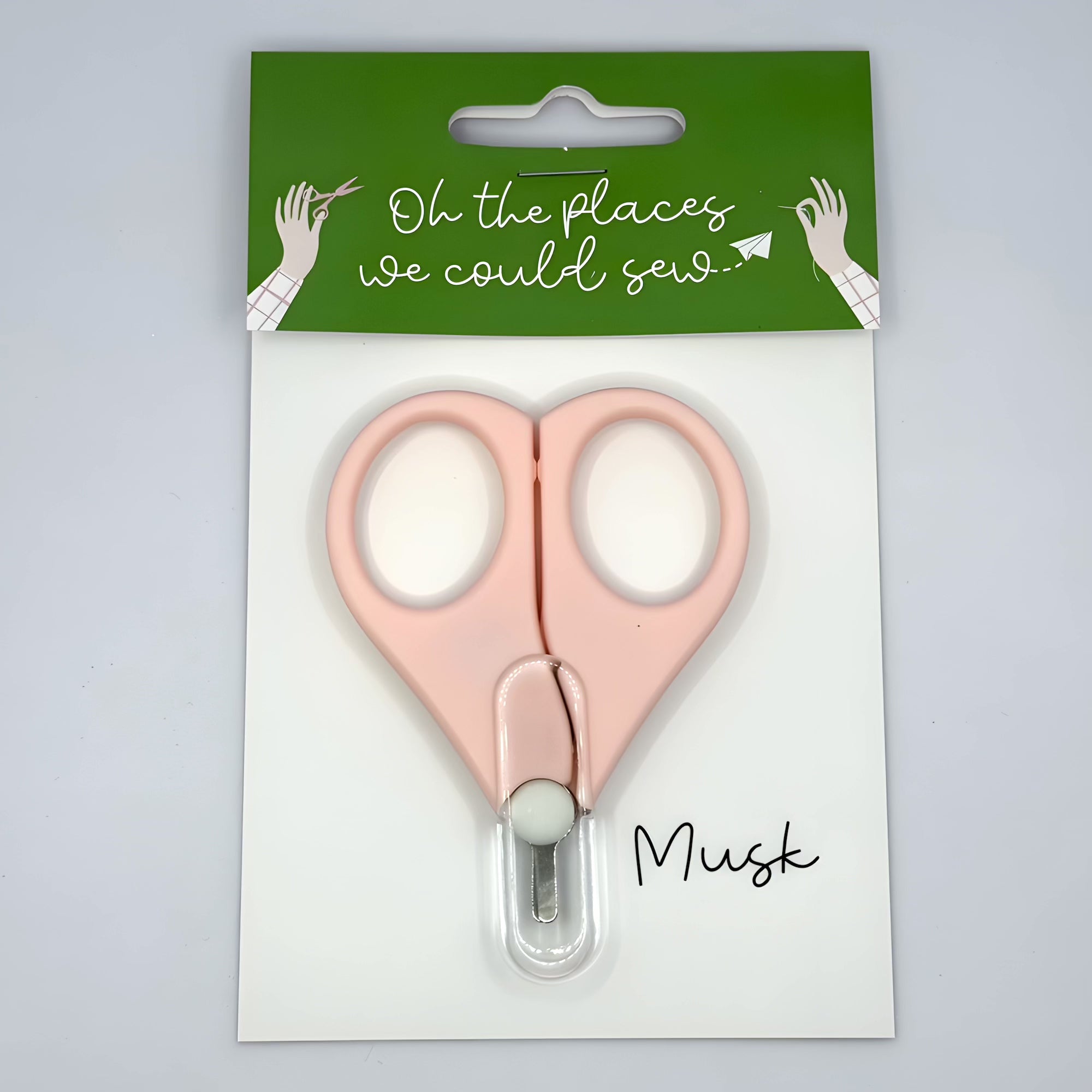 Pink scissors in packaging with 'Oh the places we could sew' text on a green label.