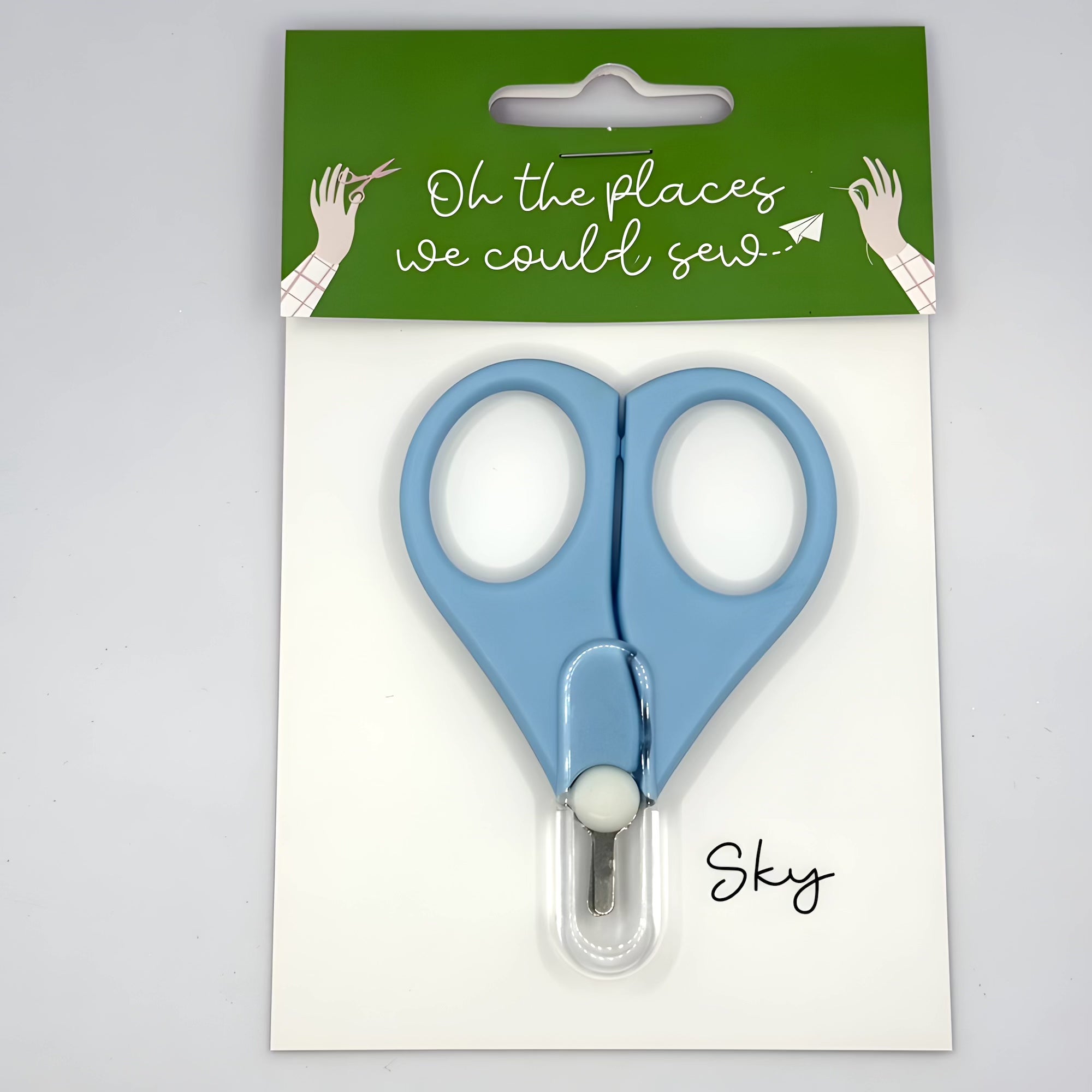 Blue scissors in packaging with 'Oh the places we could sew' text on a green label.